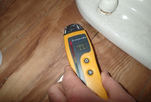 Floor shows saturation and buckling around rear of toilet in upstairs bathroom above downstairs bathroom